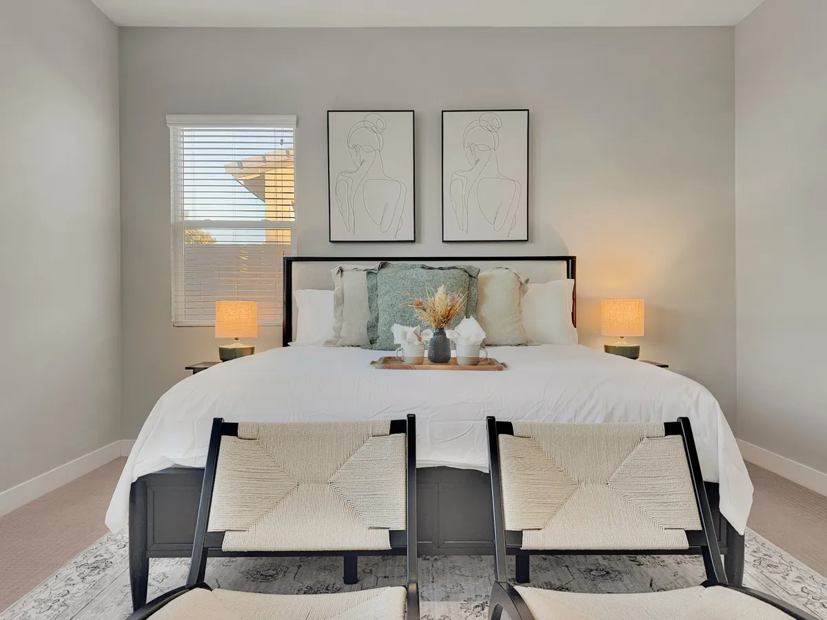 A serene bedroom featuring a plush bed with decorative pillows, minimalist art pieces above the headboard, stylish bedside lamps, and a wooden tray with decorative items. The room exudes calm with soft, neutral tones and cozy textures.