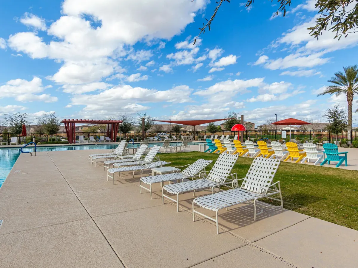 A vibrant community swimming pool surrounded by colorful lounge chairs, palm trees, and canopy shade structures. The atmosphere is cheerful and inviting, ideal for families and groups to relax and socialize outdoors.