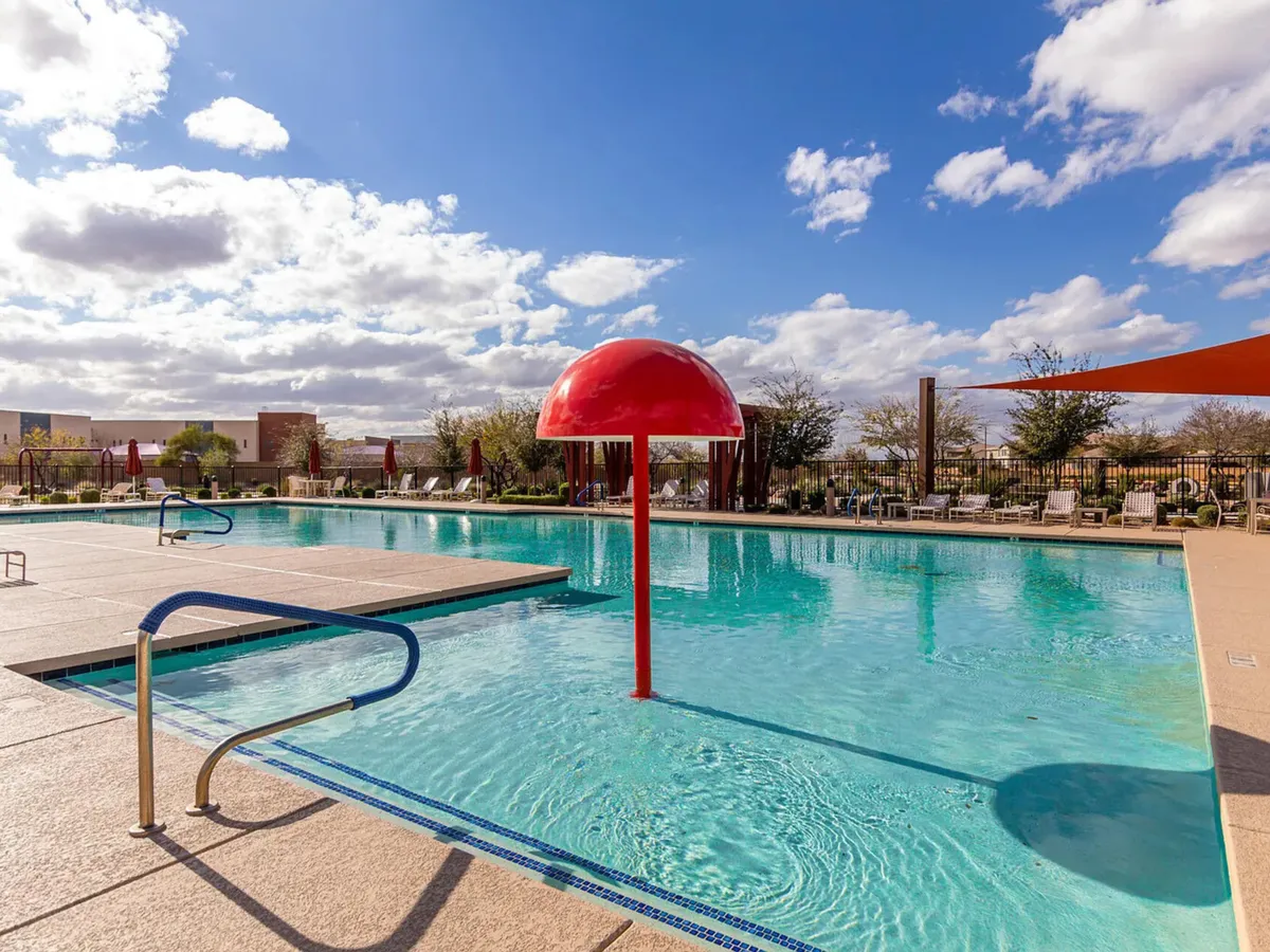 A sparkling swimming pool with a playful red water feature takes center stage. Comfortable lounge chairs and shaded structures surround the area, creating an inviting space for both socializing and relaxation. Children are seen enjoying the water, while adults relax nearby, capturing the feel of a resort-style amenity.