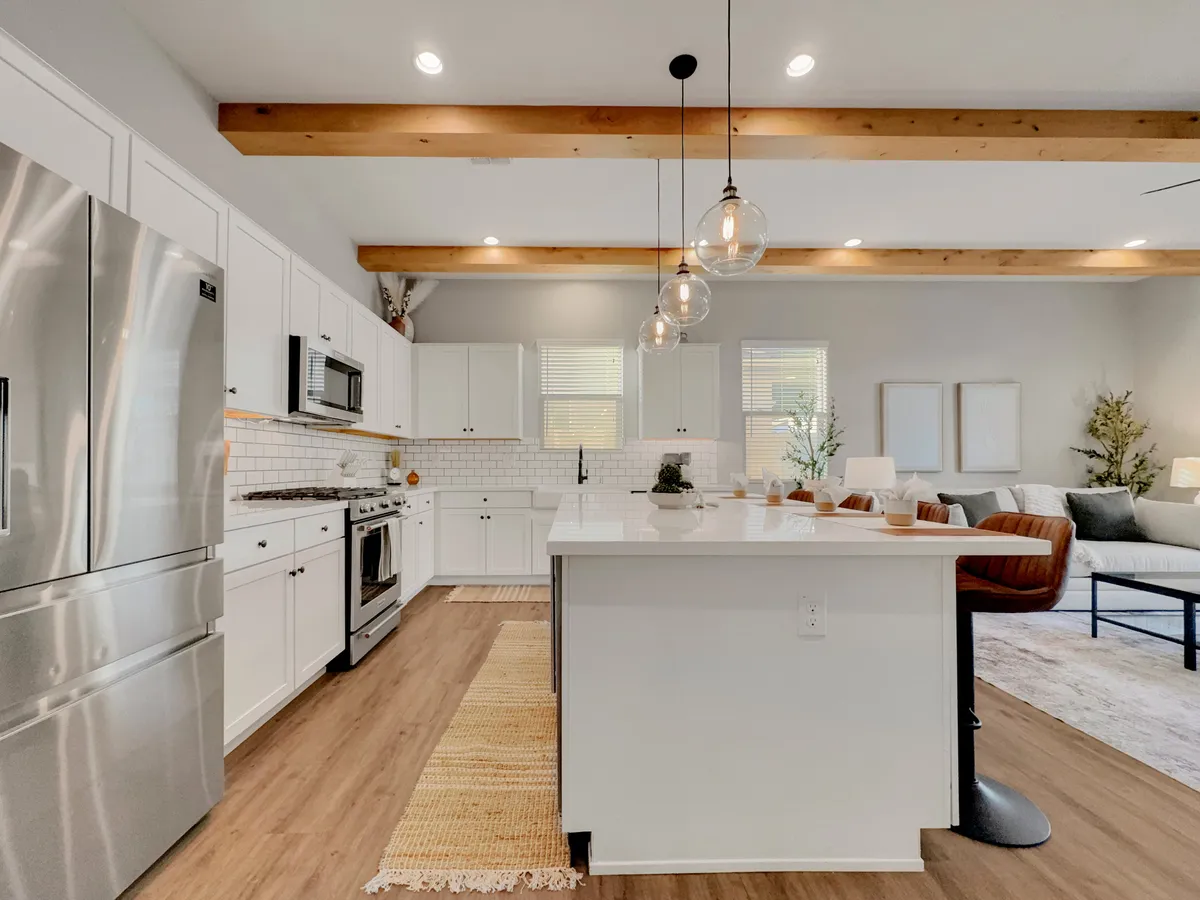 A welcoming kitchen scene with a generous island countertop, stainless steel appliances, wooden ceiling beams, pendant lighting, and comfortable seating nearby. The setup exudes warmth and functionality, ideal for entertaining guests or preparing family-style meals.