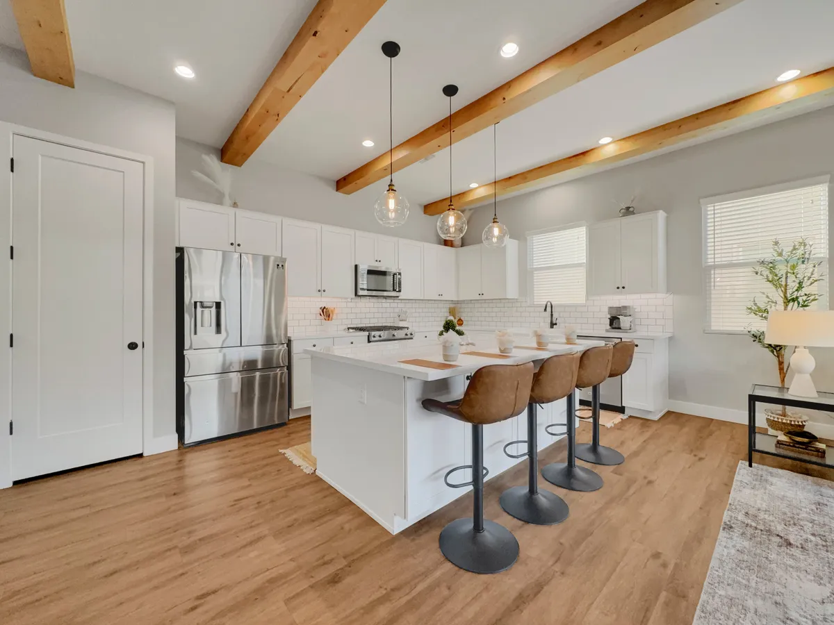 A contemporary kitchen featuring a spacious island with pendant lights above, bar stools for seating, and a suite of stainless steel appliances. The open-concept layout connects seamlessly to other living spaces, highlighting the kitchen's role as a social hub. Sleek countertops and ample workspace invite both casual meal prep and group cooking sessions.