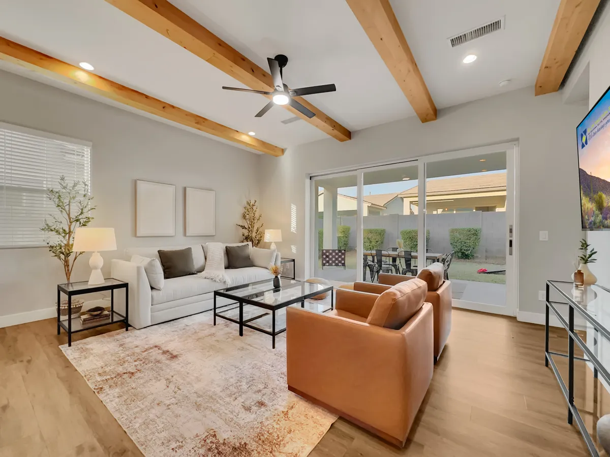 A modern living room setup featuring a plush sofa, a coffee table, a large TV, and a view through wide windows to the outdoors. The decor is streamlined, and the space is bathed in natural light, inviting both relaxation and group activities like movie nights.