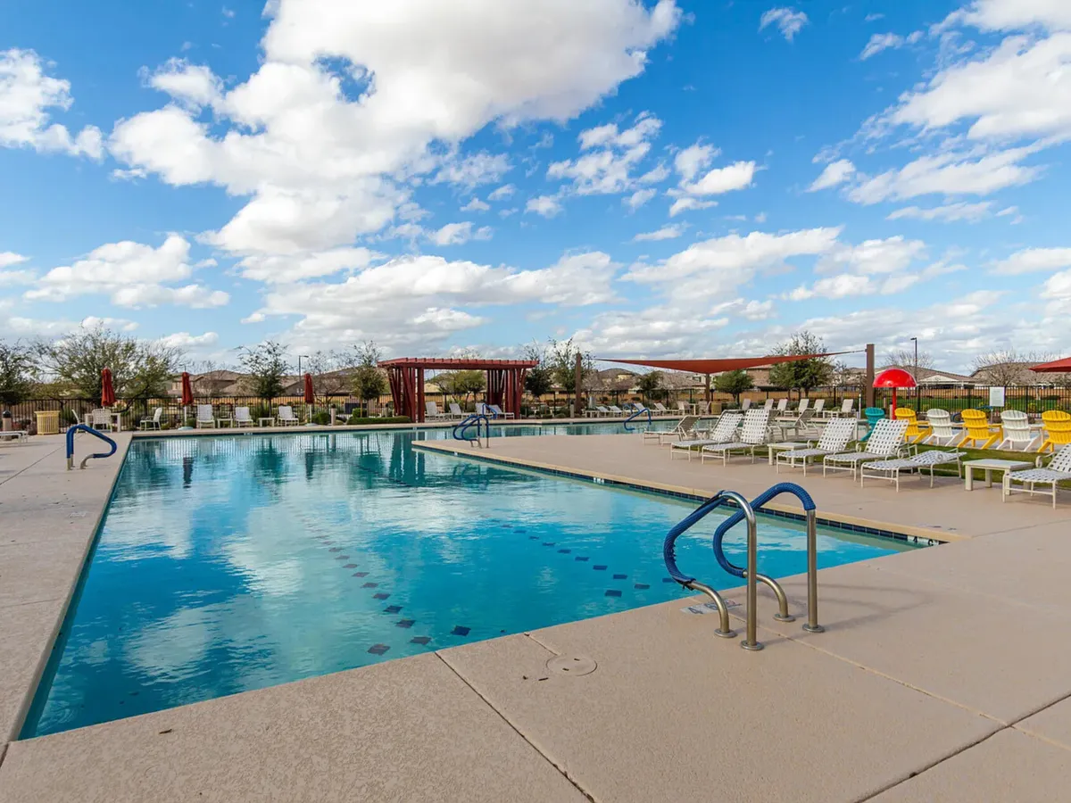 A modern swimming pool is surrounded by lounge chairs and a canopy structure, perfect for sunbathing or unwinding in the shade. The clear blue water looks inviting, and the pool area is well-kept, reflecting a leisurely and upscale community atmosphere.