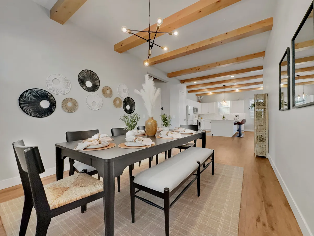 A stylish dining area with a modern table set for a meal, decorative wall plates, a chandelier light fixture, benches with cushions, and greenery in vases. The space exudes warmth and is perfectly suited for shared meals and gatherings.